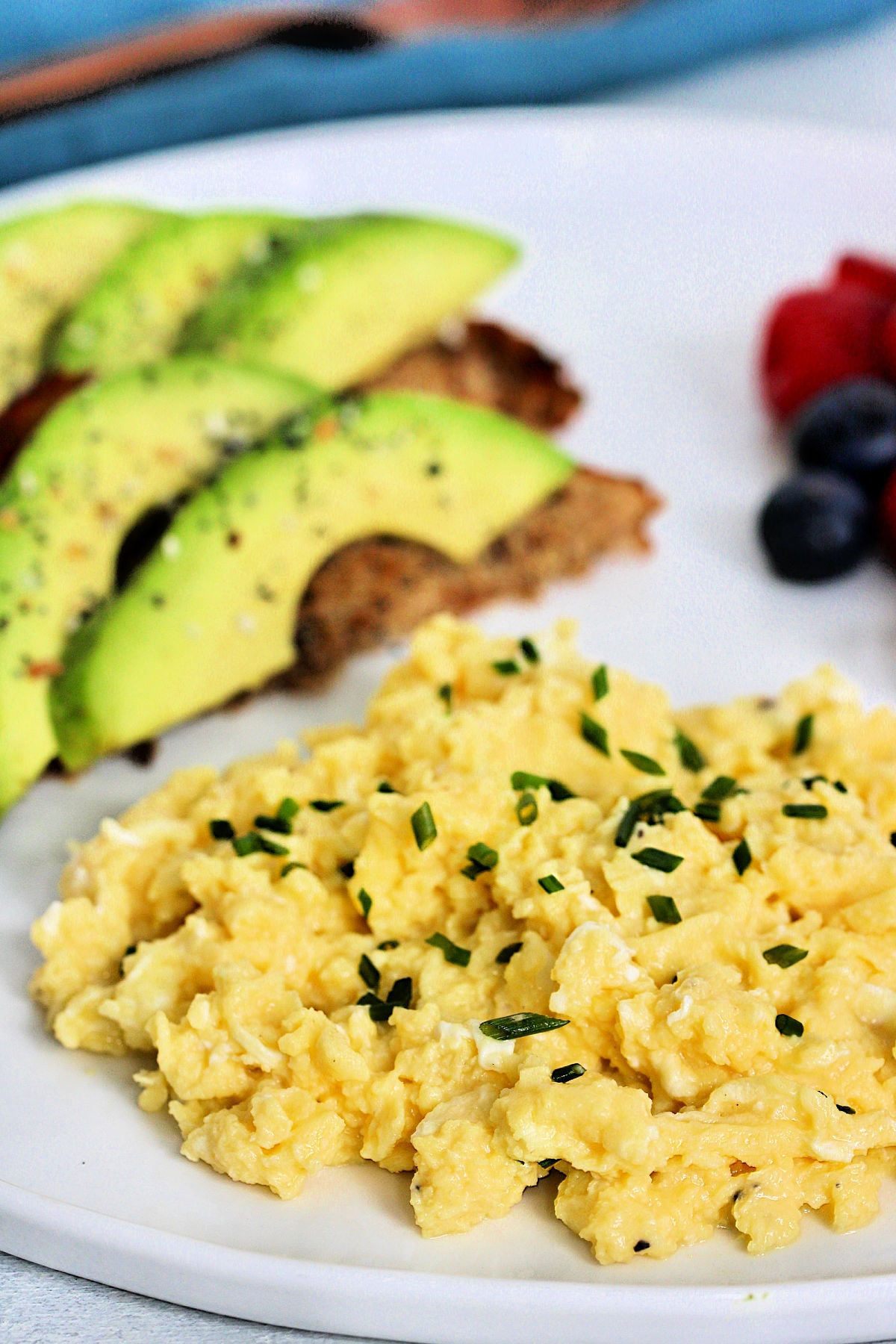 High protein scrambled eggs with cottage cheese on white plate with avocado toast and mixed berries