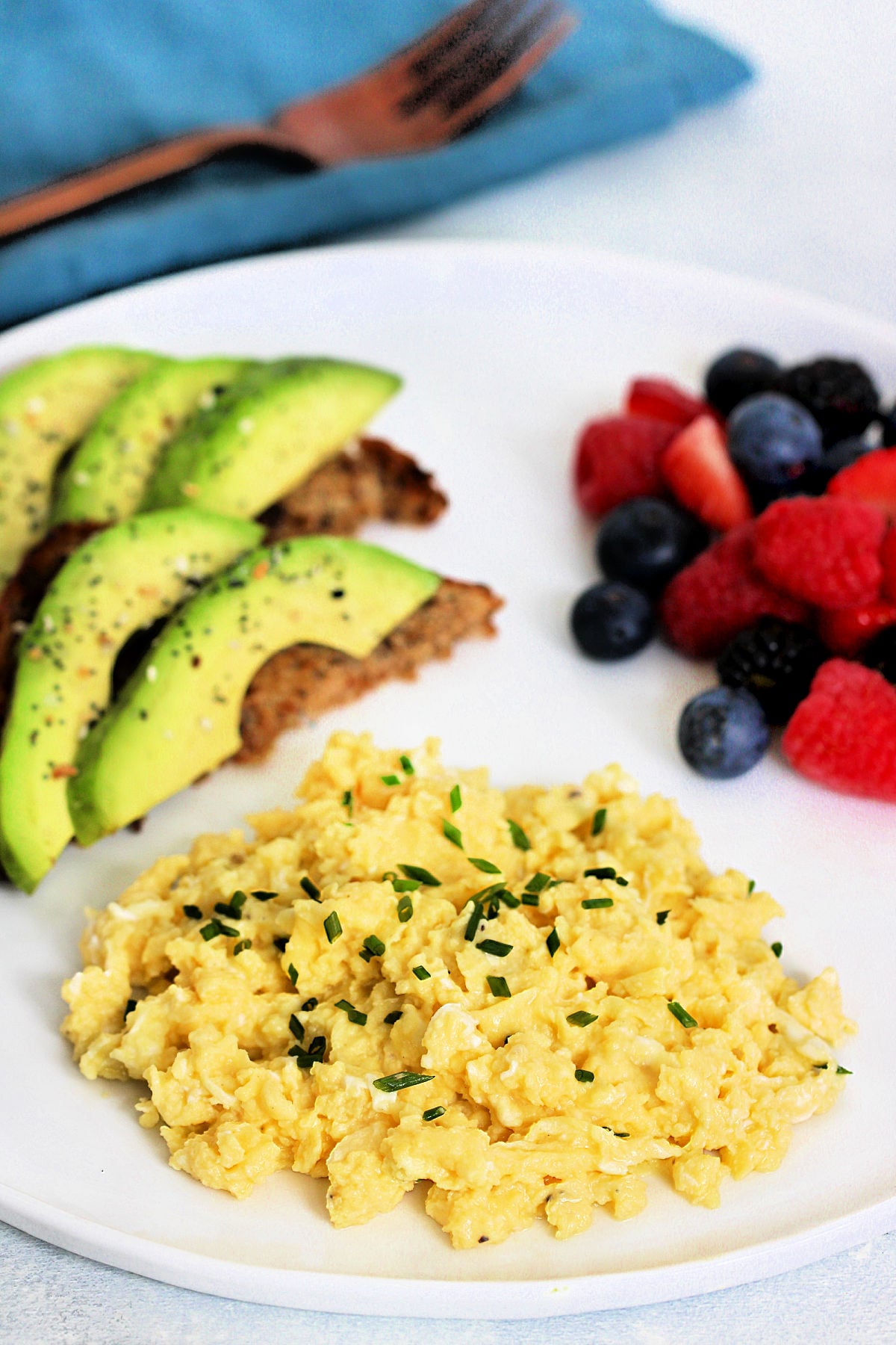 High protein scrambled eggs with cottage cheese on white plate with avocado toast and mixed berries