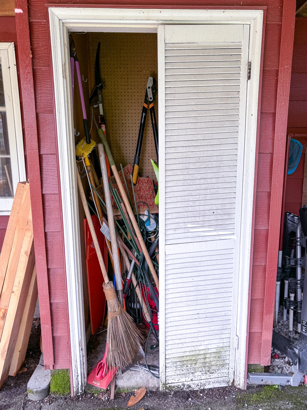 small garden shed with tools inside and broken louvered door