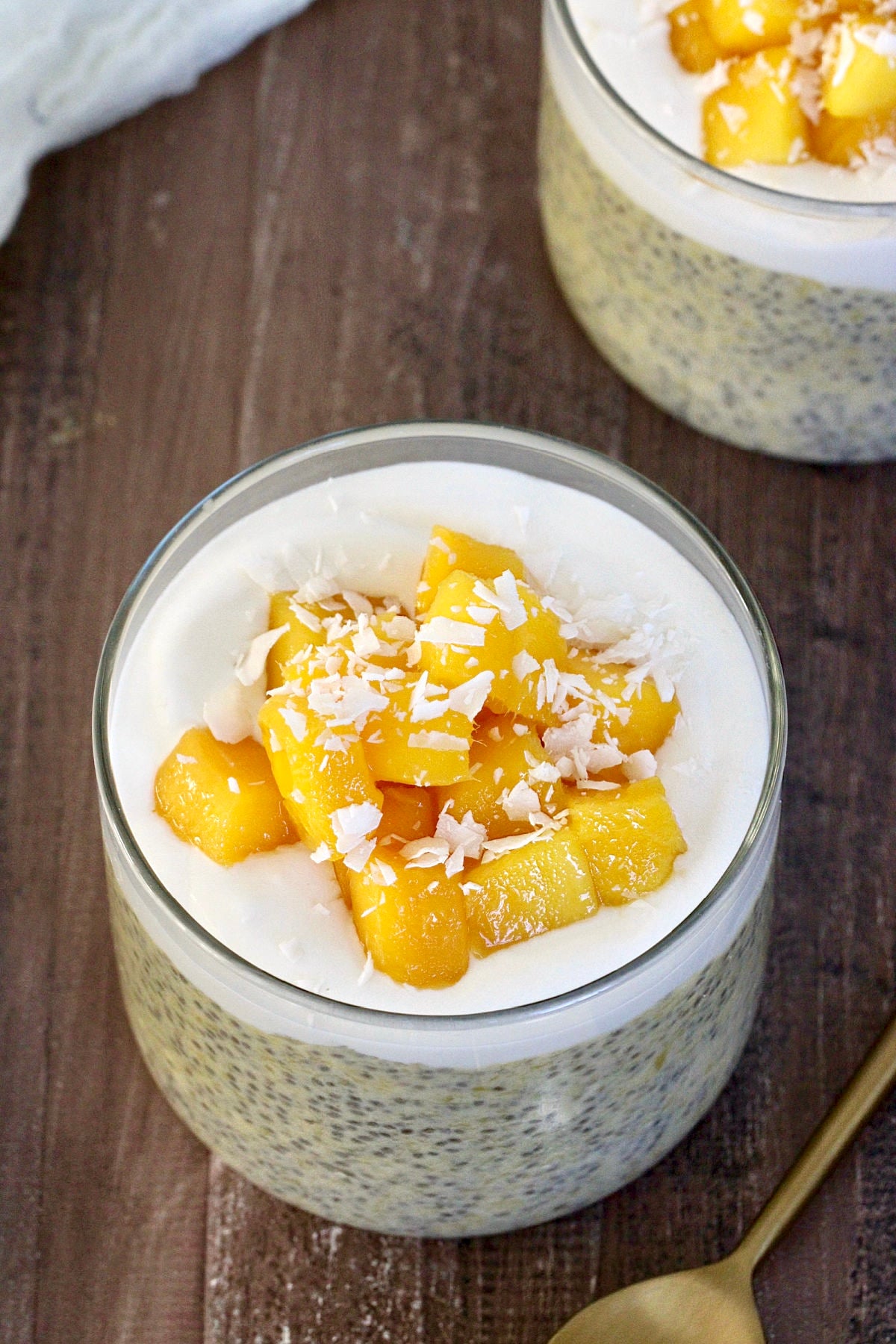 Mango Chia Pudding in a glass jar with a gold spoon nearby.