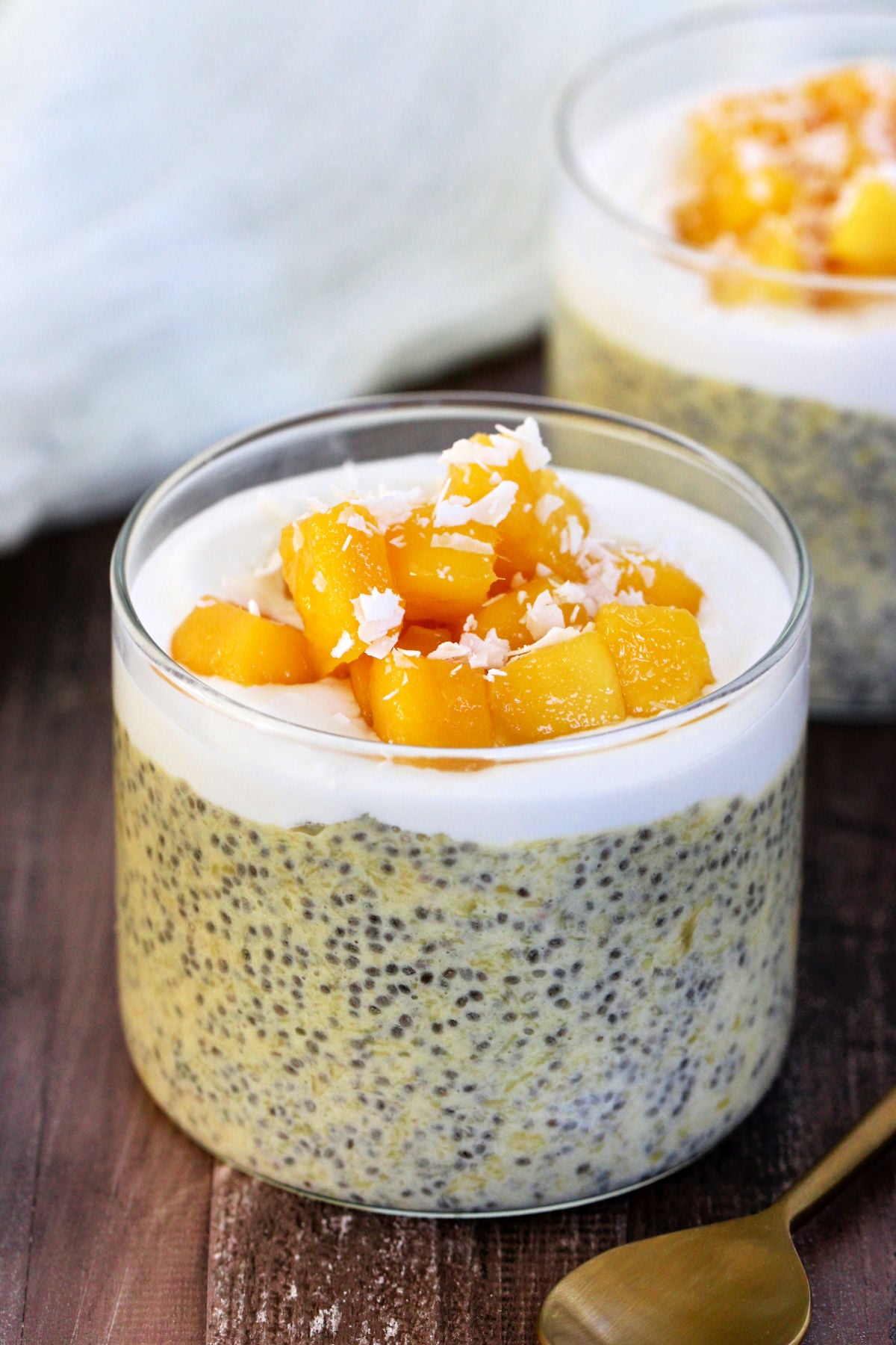 Mango Chia Pudding in a glass jar with a gold spoon nearby.