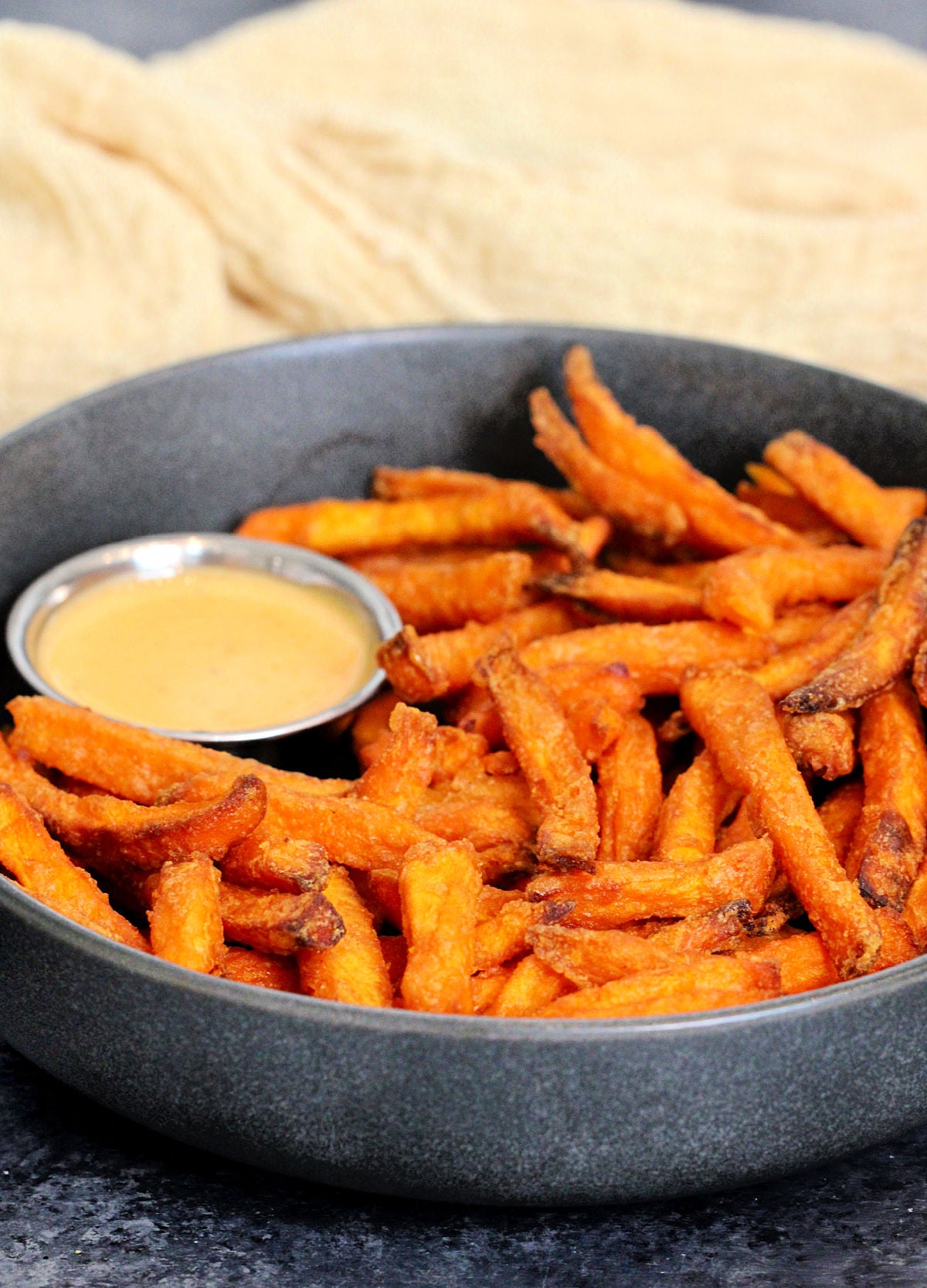 A bowl of air fryer sweet potato fries with a cup of dipping sauce.