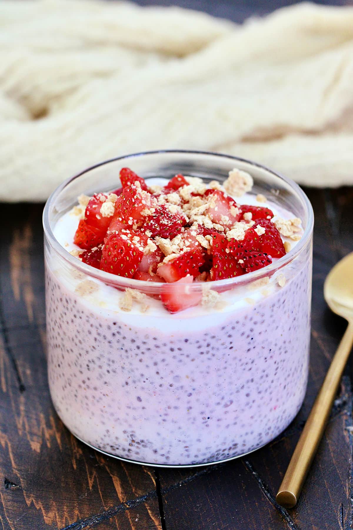 Strawberry cheesecake chia pudding in a glass topped with fresh strawberries and crumbled graham crackers.