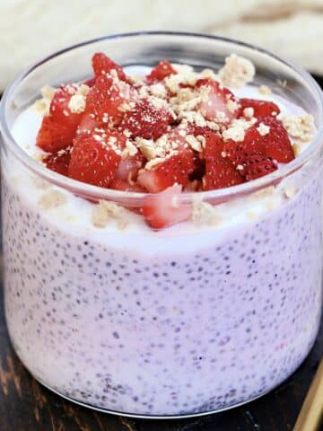 Strawberry cheesecake chia pudding in a glass topped with fresh strawberries and crumbled graham crackers.