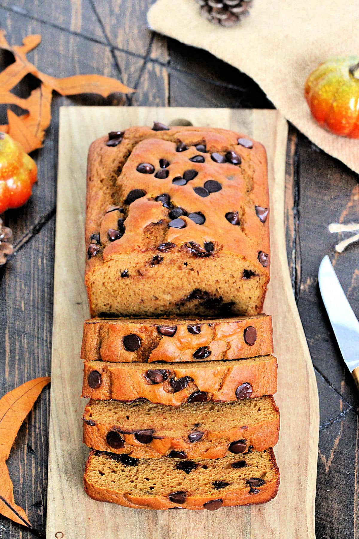 A loaf of high protein pumpkin chocolate chip bread on a wooden board cut into several slices.