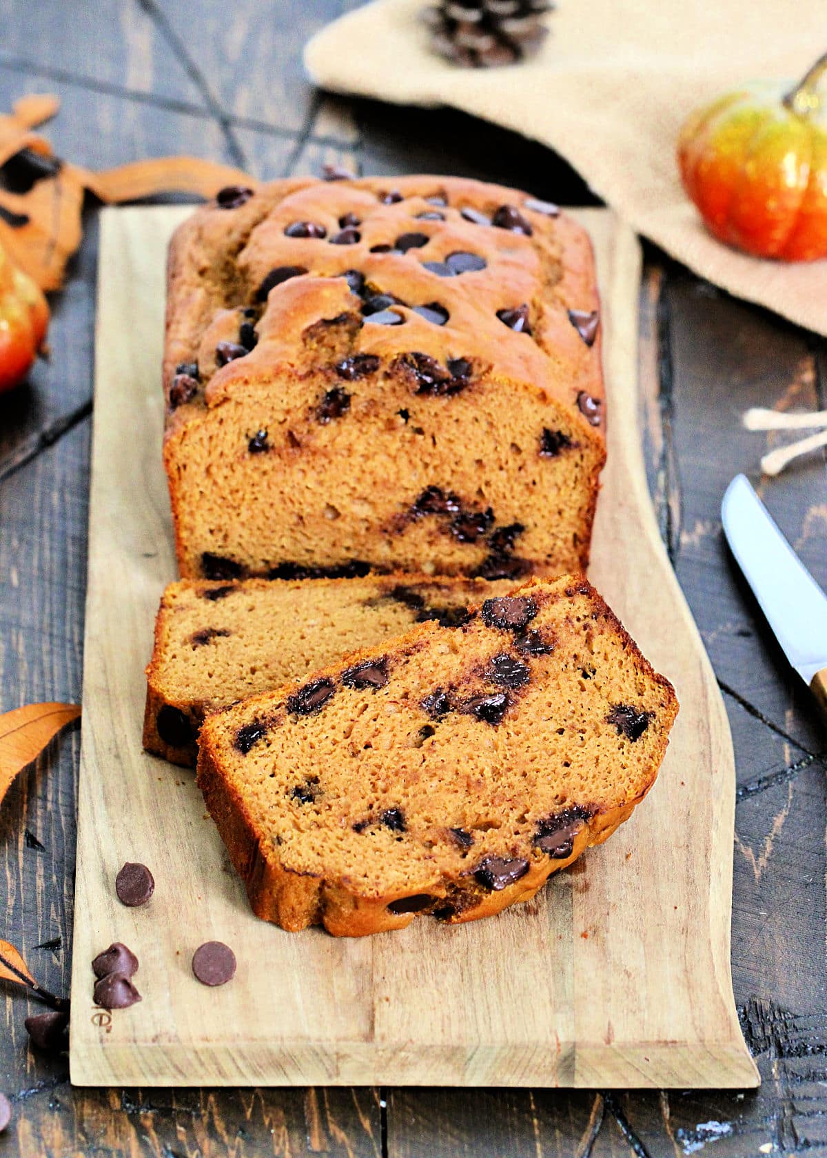 A loaf of high protein pumpkin chocolate chip bread on a wooden board with two cut slices nearby.