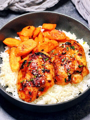 Miso chicken thighs with roasted carrots and white rice in a black bowl.