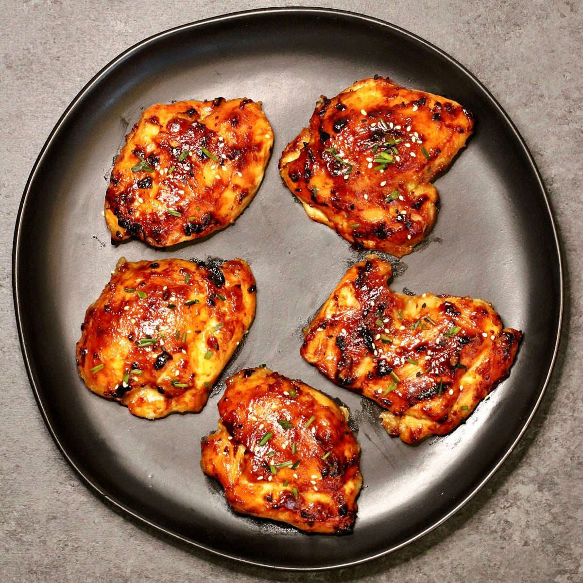 Miso chicken thighs on a black plate.