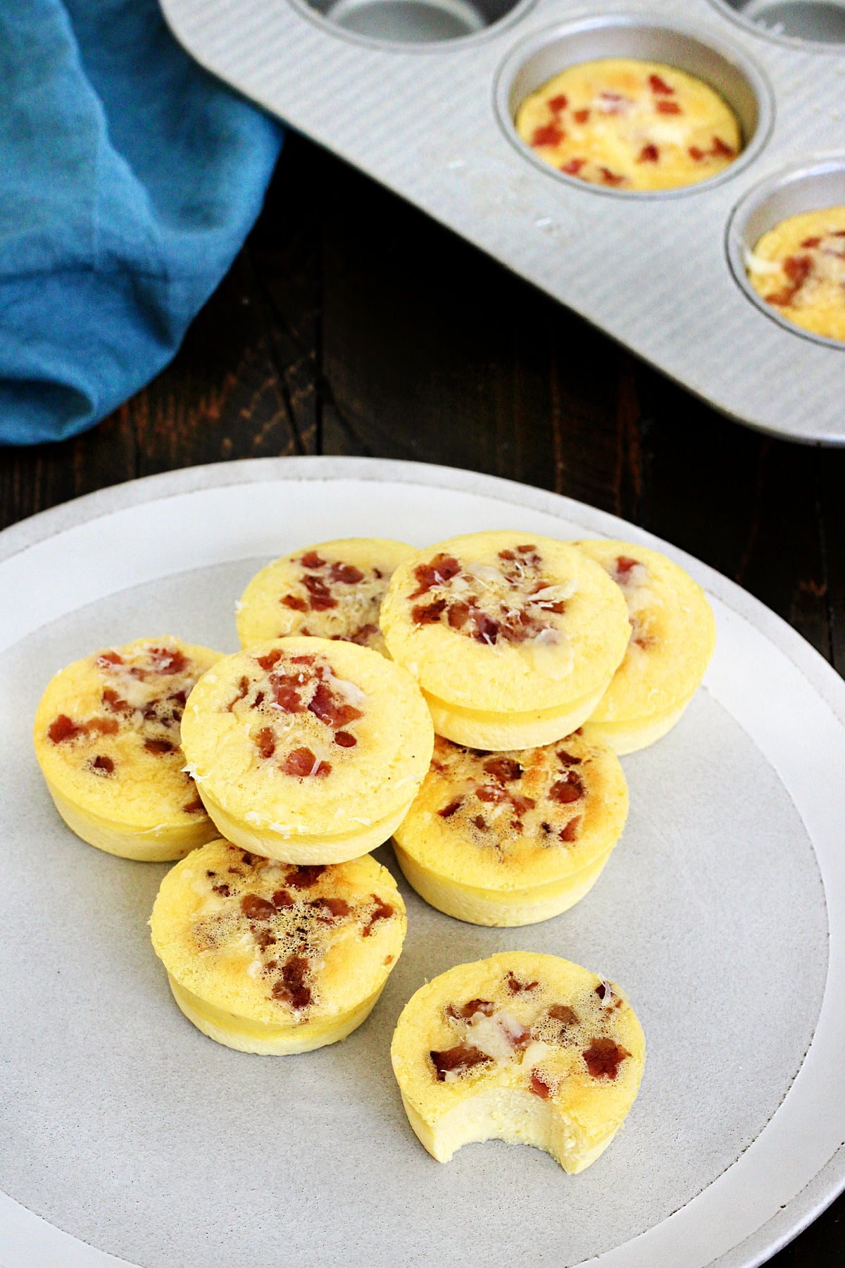 A stack of Starbucks copycat egg bites with bacon on a plate, one has a bite taken out of it.
